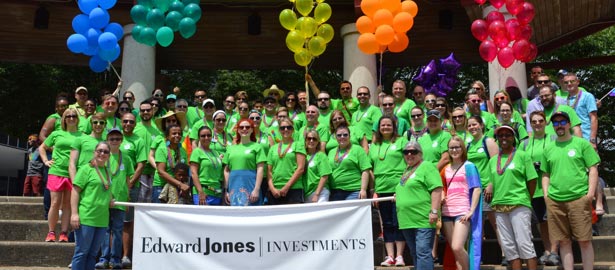 A large group of associates in green t-shirts stand behind an Edward Jones Investment banner.